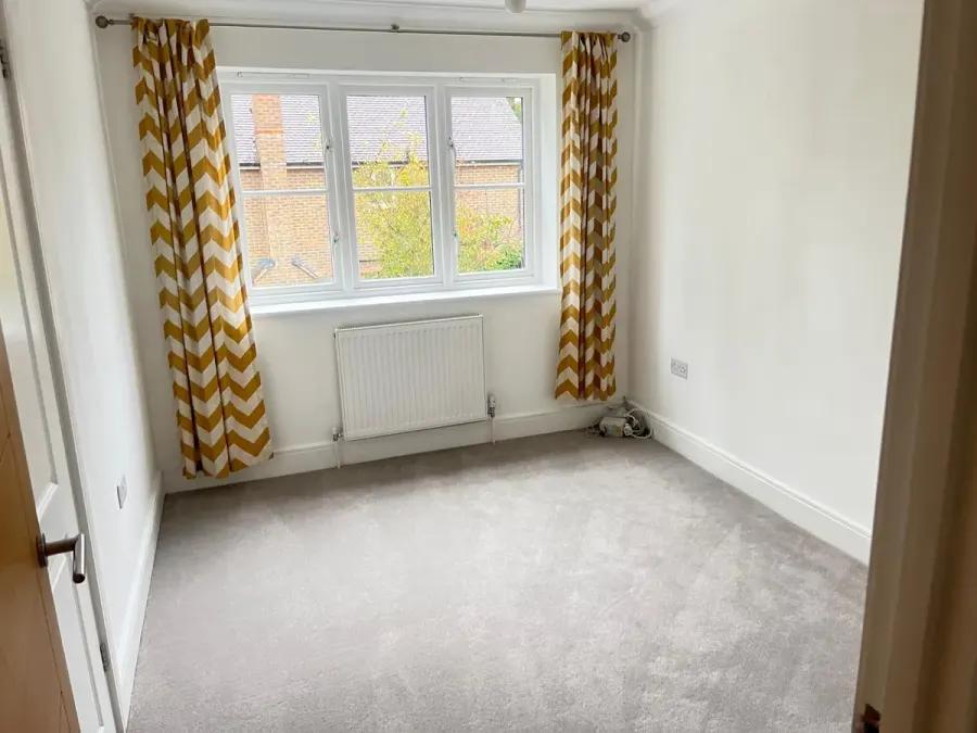 Freshly cleaned bedroom with a grey carpet, radiator and yellow curtains